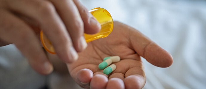Person puts pills from prescription bottle into their hand