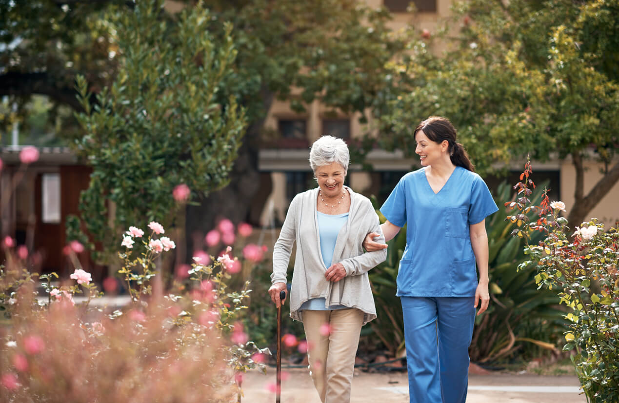 Woman and elderly woman walking outside of a nursing home.
