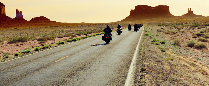 A desert background, with motorcyclists riding on the road