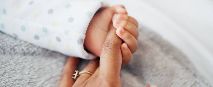 Newborn baby holding finger of mother
